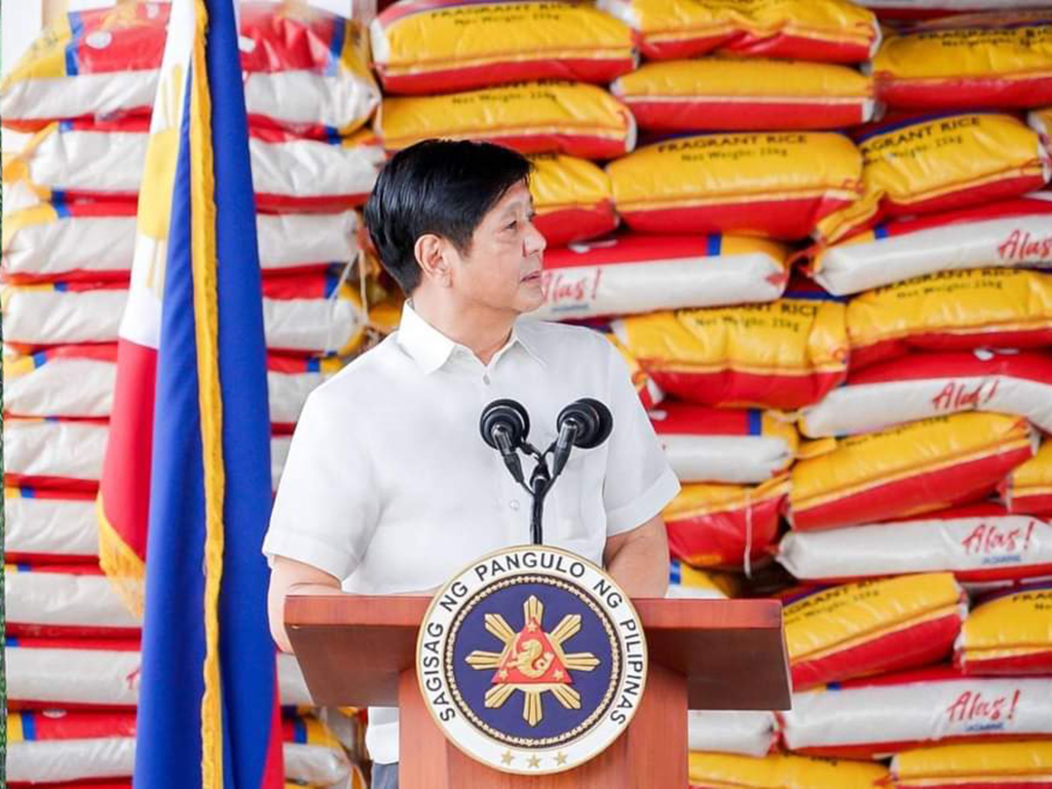 President Marcos Jr. in front of rice bags during a speech in San Jose, Dinagat Islands